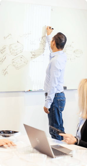 team in boardroom watching 1 person draw product illustrations on whiteboard