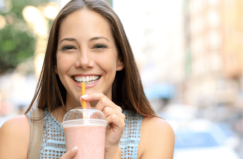 closeup of woman smiling and enjoying smoothie in clear drink container with yellow straw