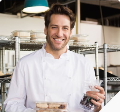 smiling chef in chefs coat standing in front of rows of baked goods in packages