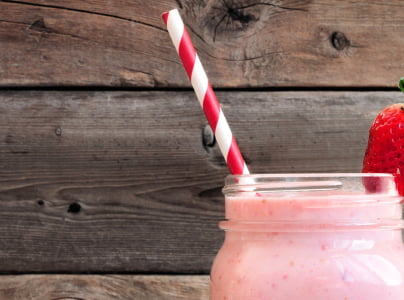 strawberry milkshake in clear drinking cup with multicolour paper straw