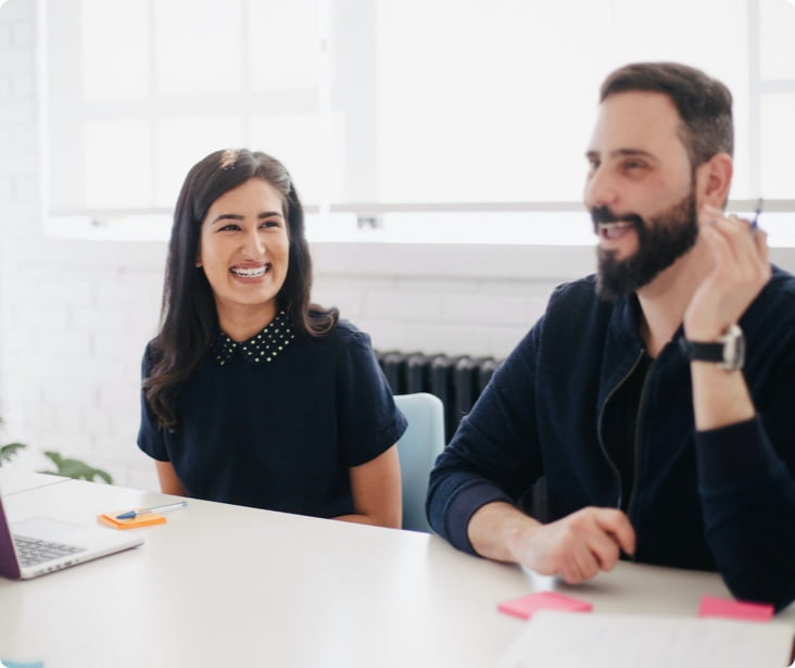 two office workers smiling and laughing at desk making sticky notes